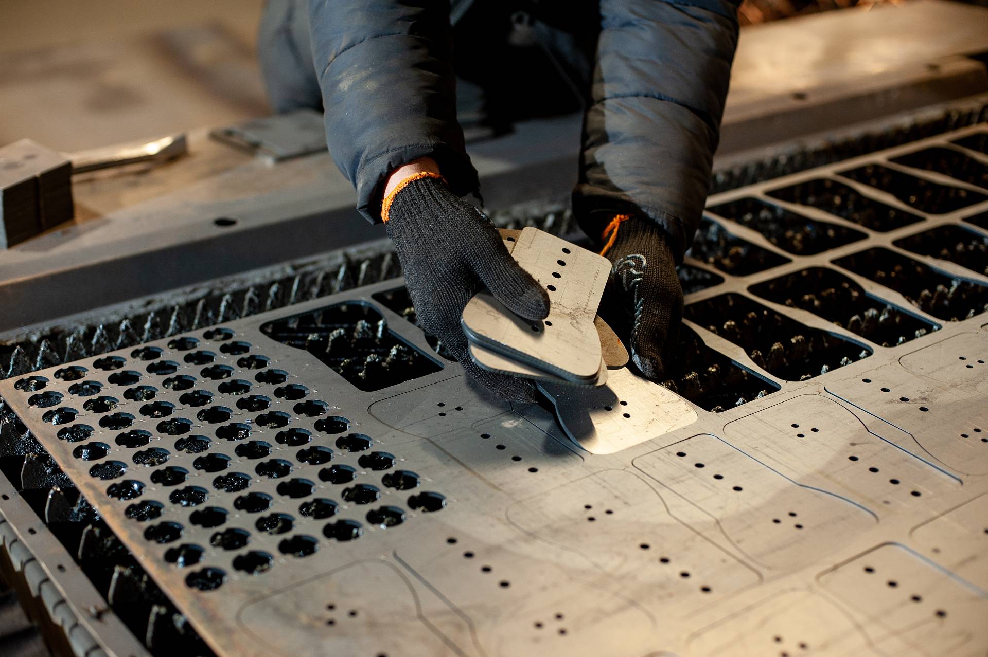 Ein Arbeiter mit Handschuhen entnimmt ein ausgestanztes Metallteil aus einer Blechtafel in einer Werkstatt.